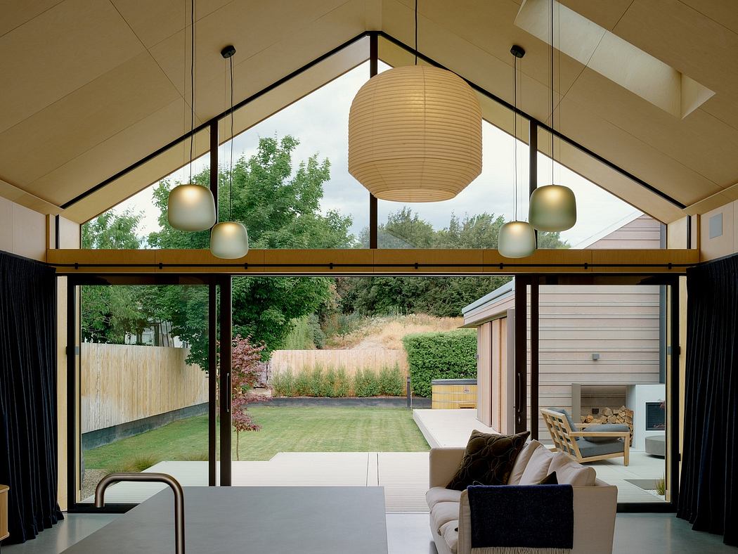 Spacious living space with vaulted ceiling, modern lighting, and panoramic glass walls overlooking lush greenery.