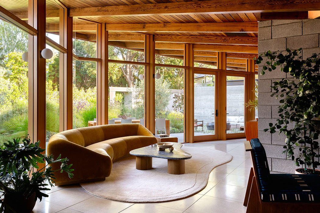 A spacious living room with wooden beams, large windows, and a curved velvet sofa.