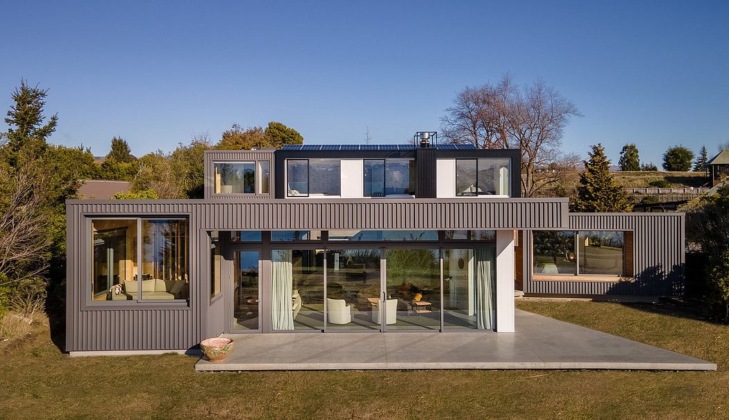 Modern, modular home with expansive windows, solar panels, and a concrete patio.