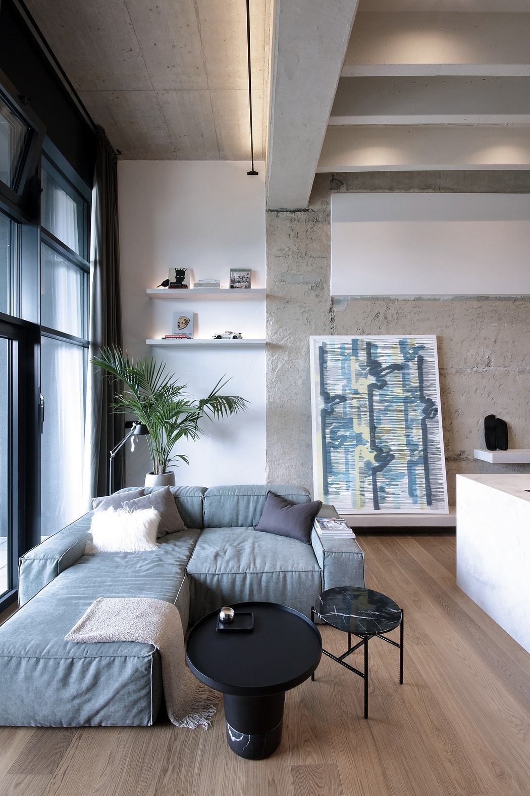 A modern living room with concrete walls, wood floors, and a gray sectional sofa.