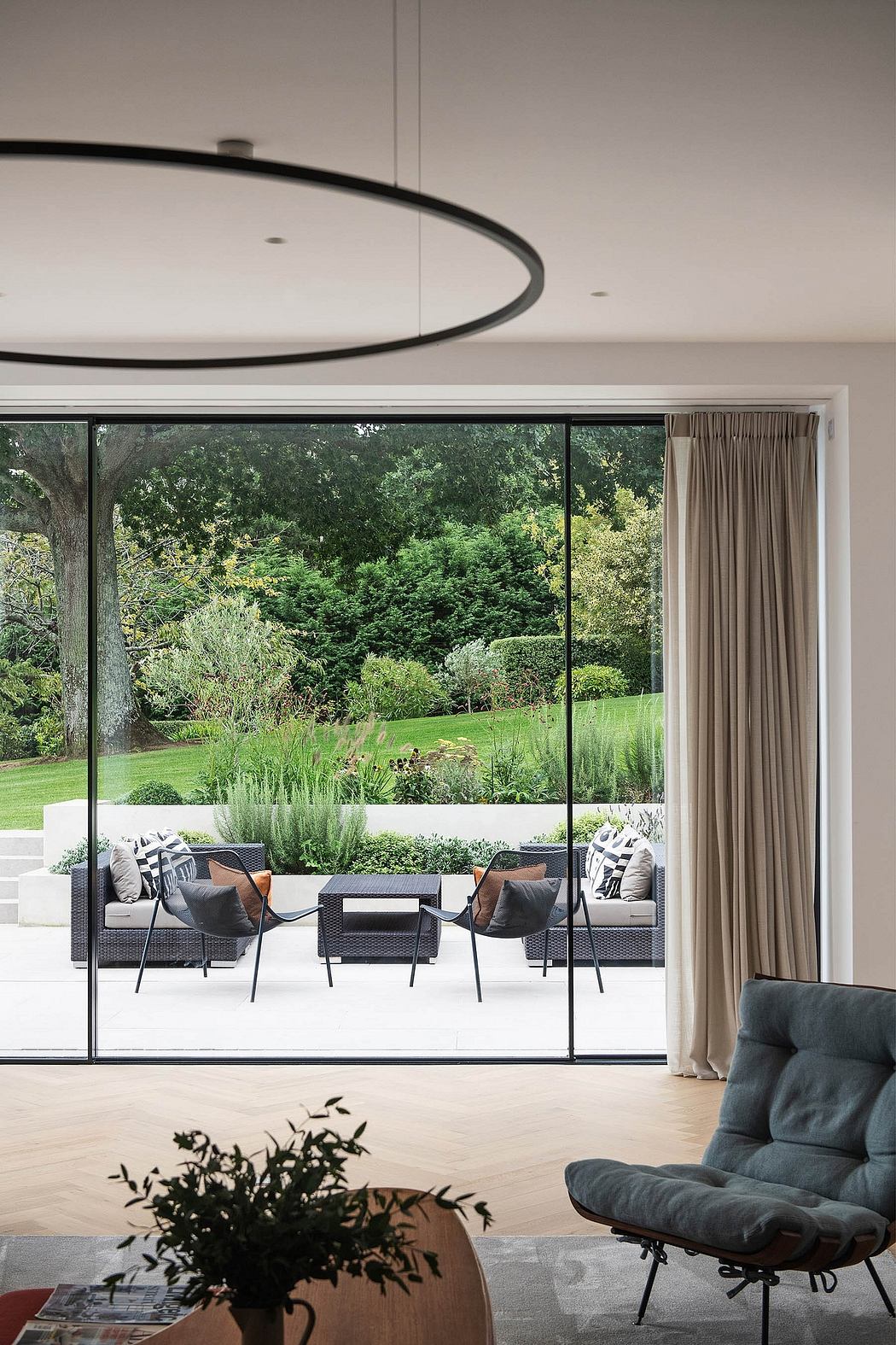 Large circular light fixture above a glass sliding door overlooking a lush garden patio.