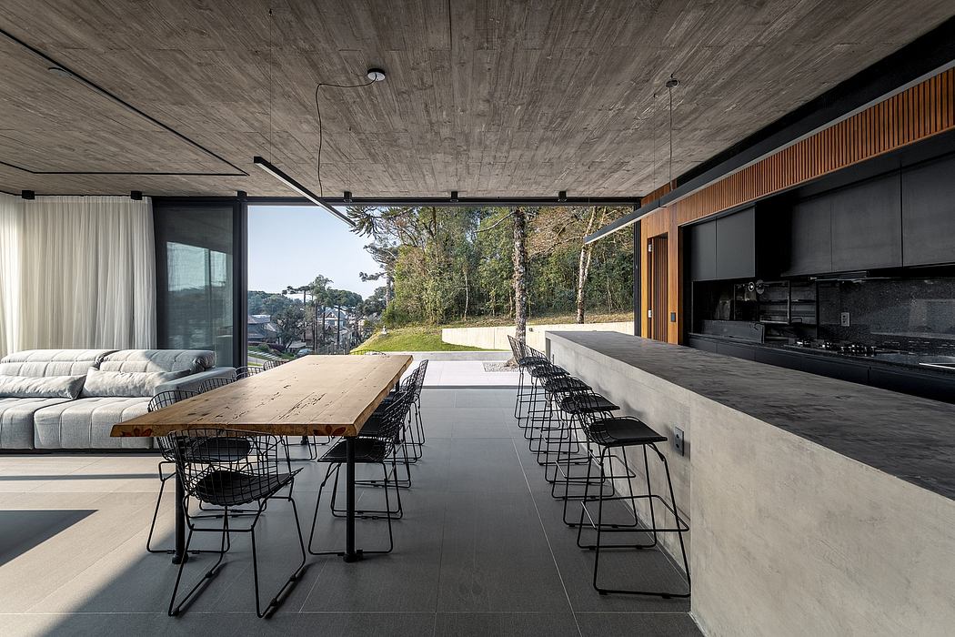 A modern, open-concept living space with a large wooden dining table, black wire chairs, and a lush outdoor view.