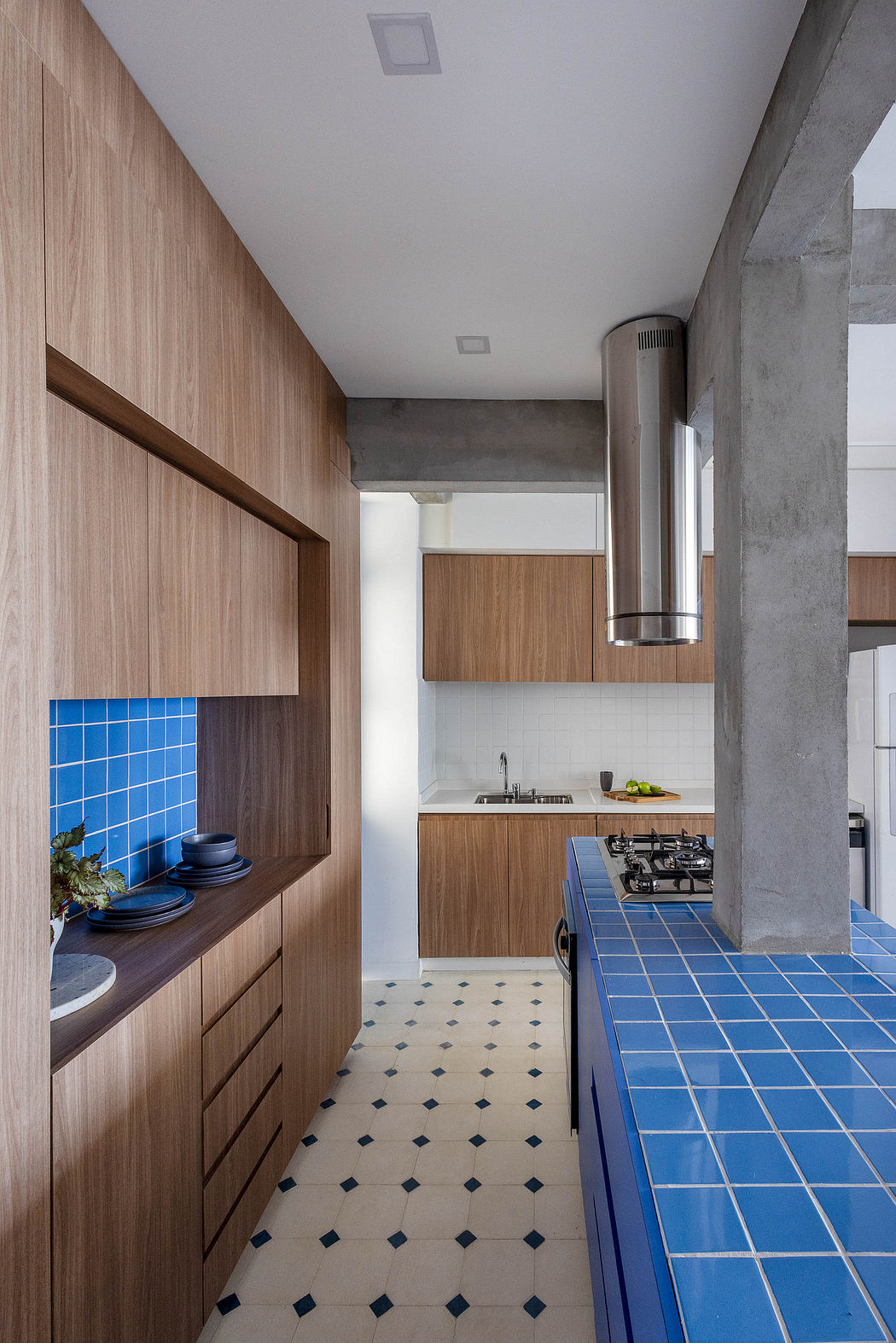 A modern kitchen with sleek wood cabinetry, bold blue tiled countertops, and a concrete ceiling.