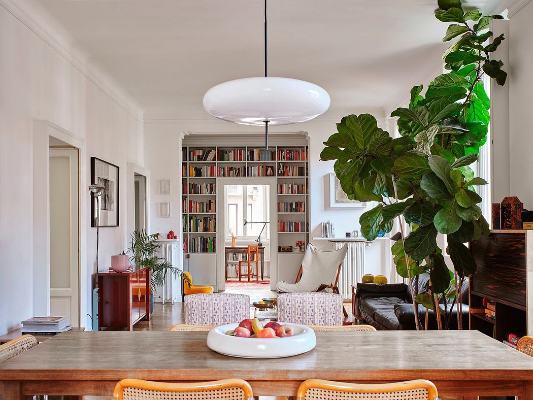 A cozy, modern living room with a large bookshelf, potted plant, and wooden dining table.