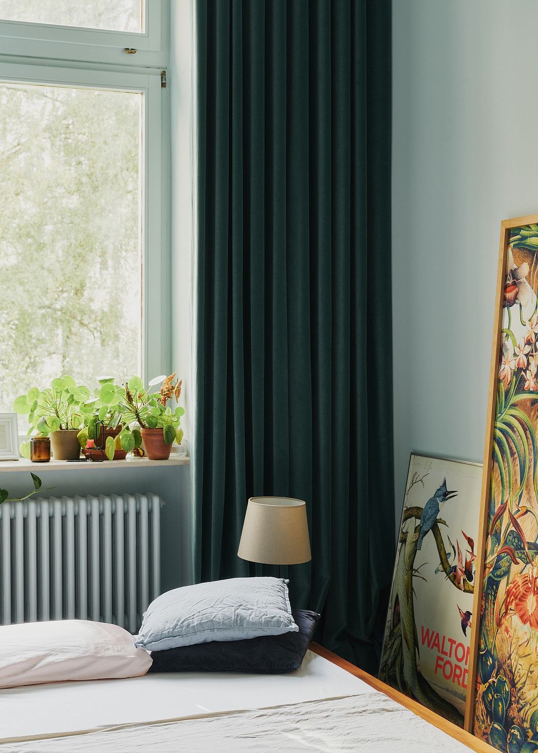 Cozy bedroom with lush plant display, decorative window curtains, and framed artwork.