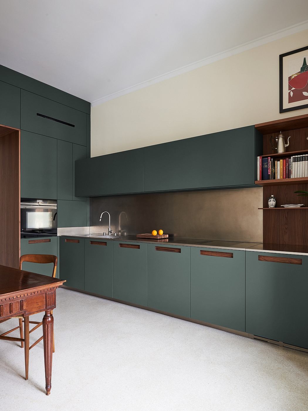 A modern kitchen with sleek, dark green cabinets and wood accents, complemented by a vintage dining table.
