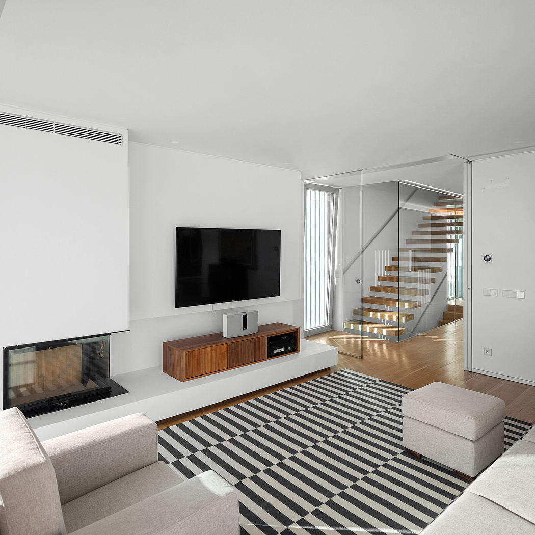 Modern living room with sleek TV stand, glass staircase, and bold striped rug.