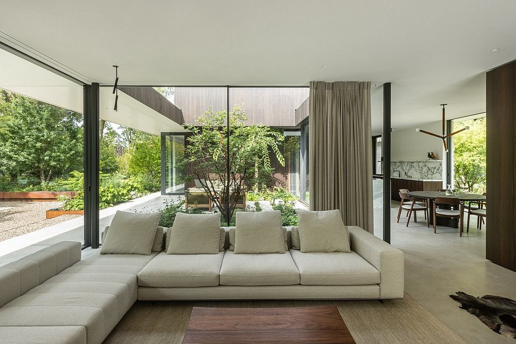An open, modern interior with a lush garden view through large windows, featuring a plush sectional sofa.