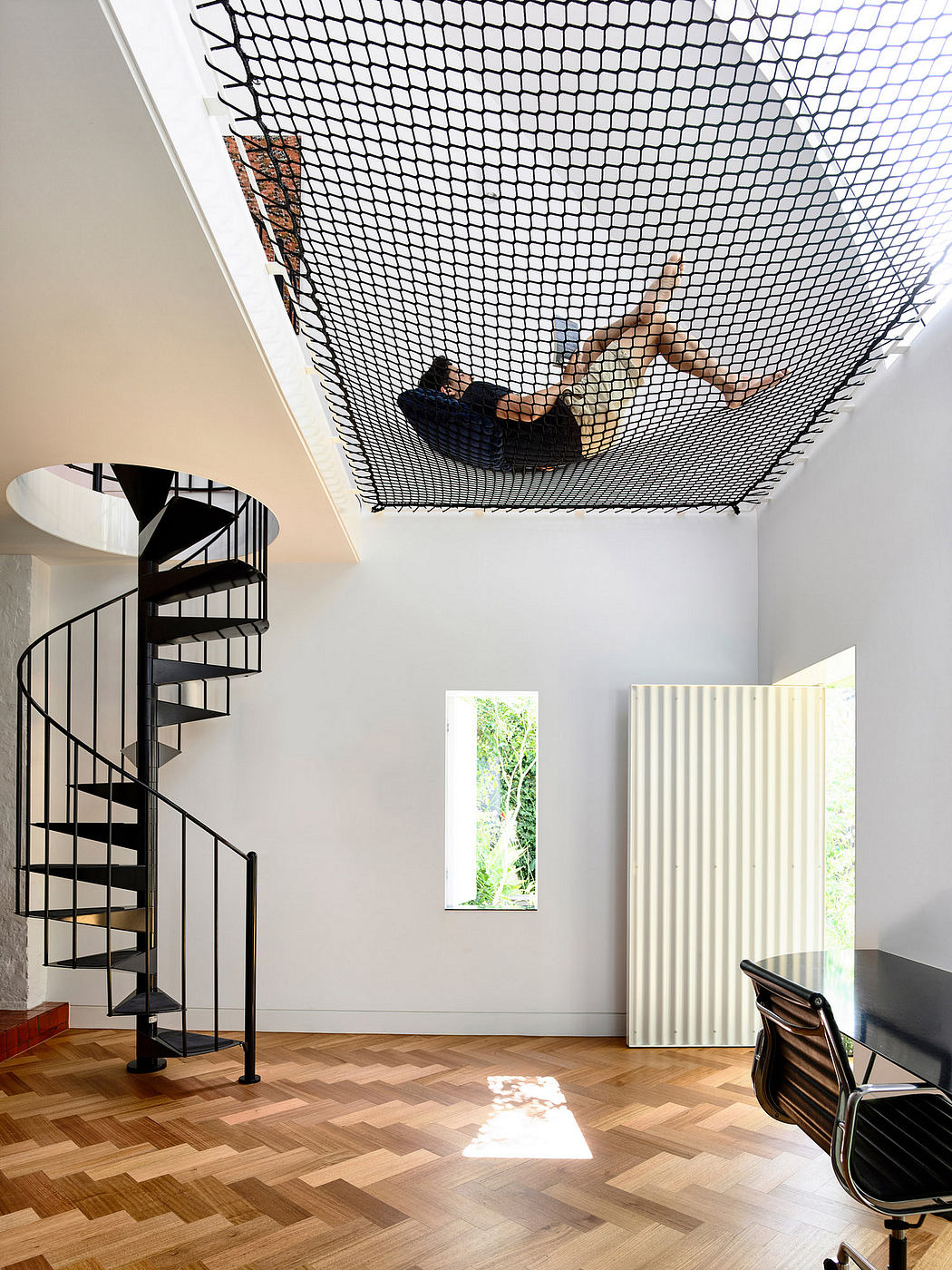 A modern interior with a spiral staircase, window, and a suspended net structure in the ceiling.