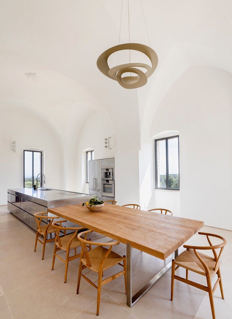 A modern, minimalist dining area with a wooden table, wishbone chairs, and a sculptural pendant light.