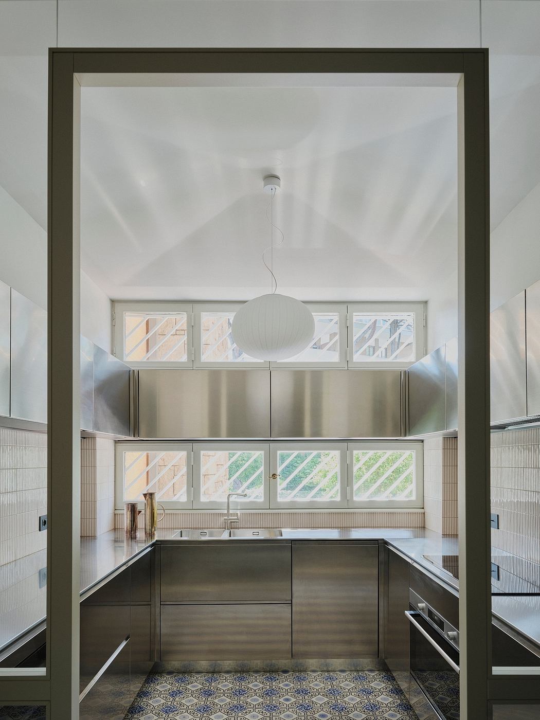 Modern kitchen with sleek stainless steel appliances, geometric tile floor, and pendant lighting.