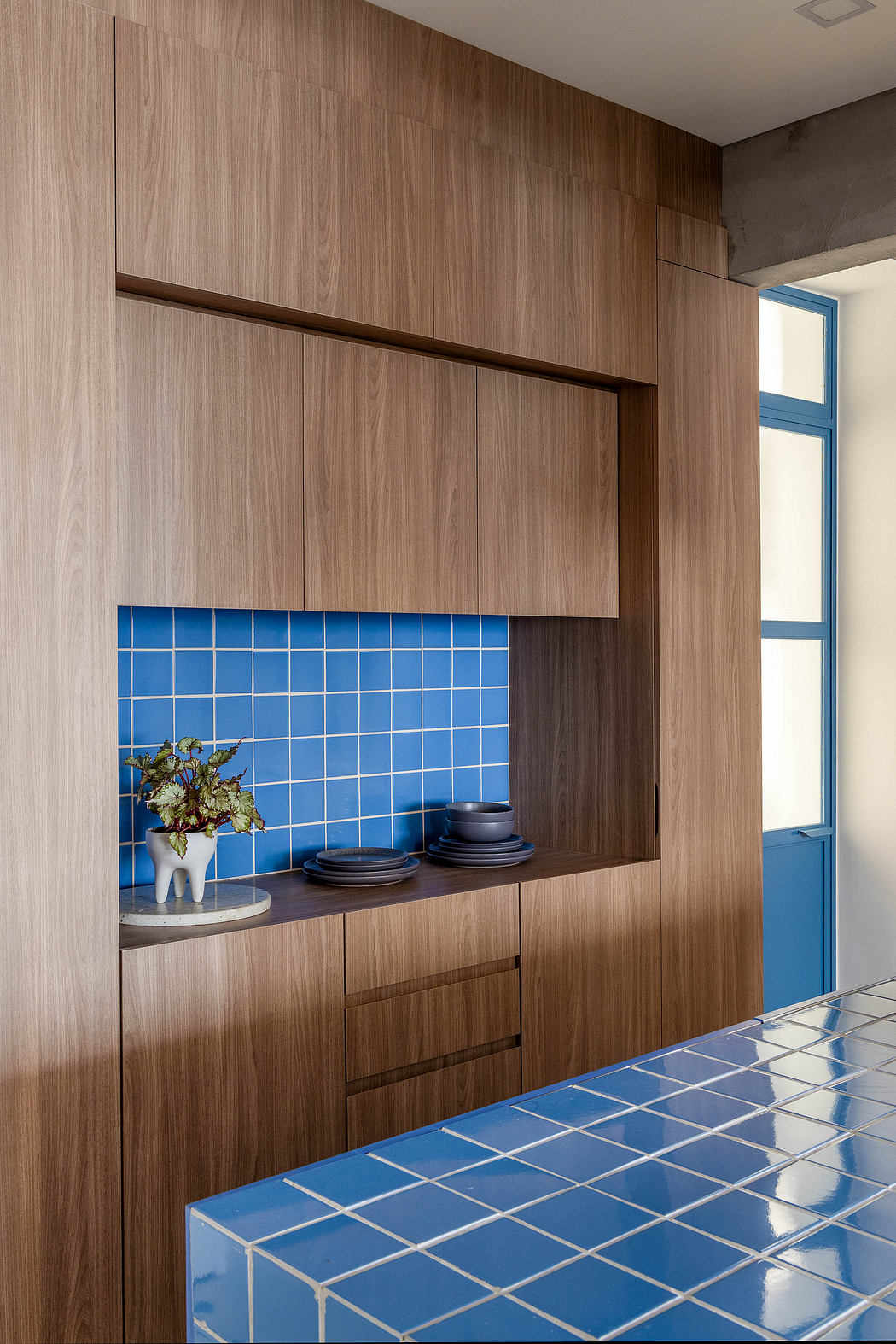 Minimalist kitchen with warm wood cabinetry, blue tiled backsplash, and sleek marble countertop.