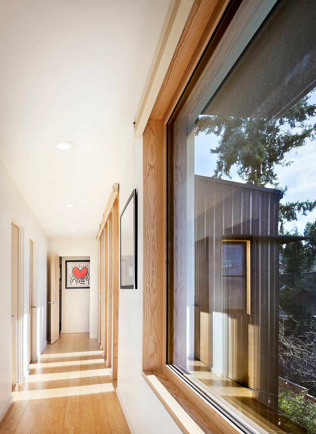 A bright, modern hallway with wooden accents, large windows, and a vibrant artwork.