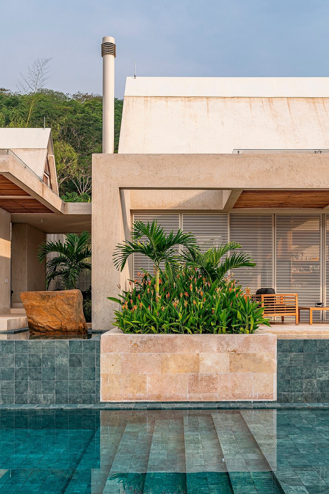 A modern tropical villa with a sleek concrete façade, lush greenery, and a reflective pool.