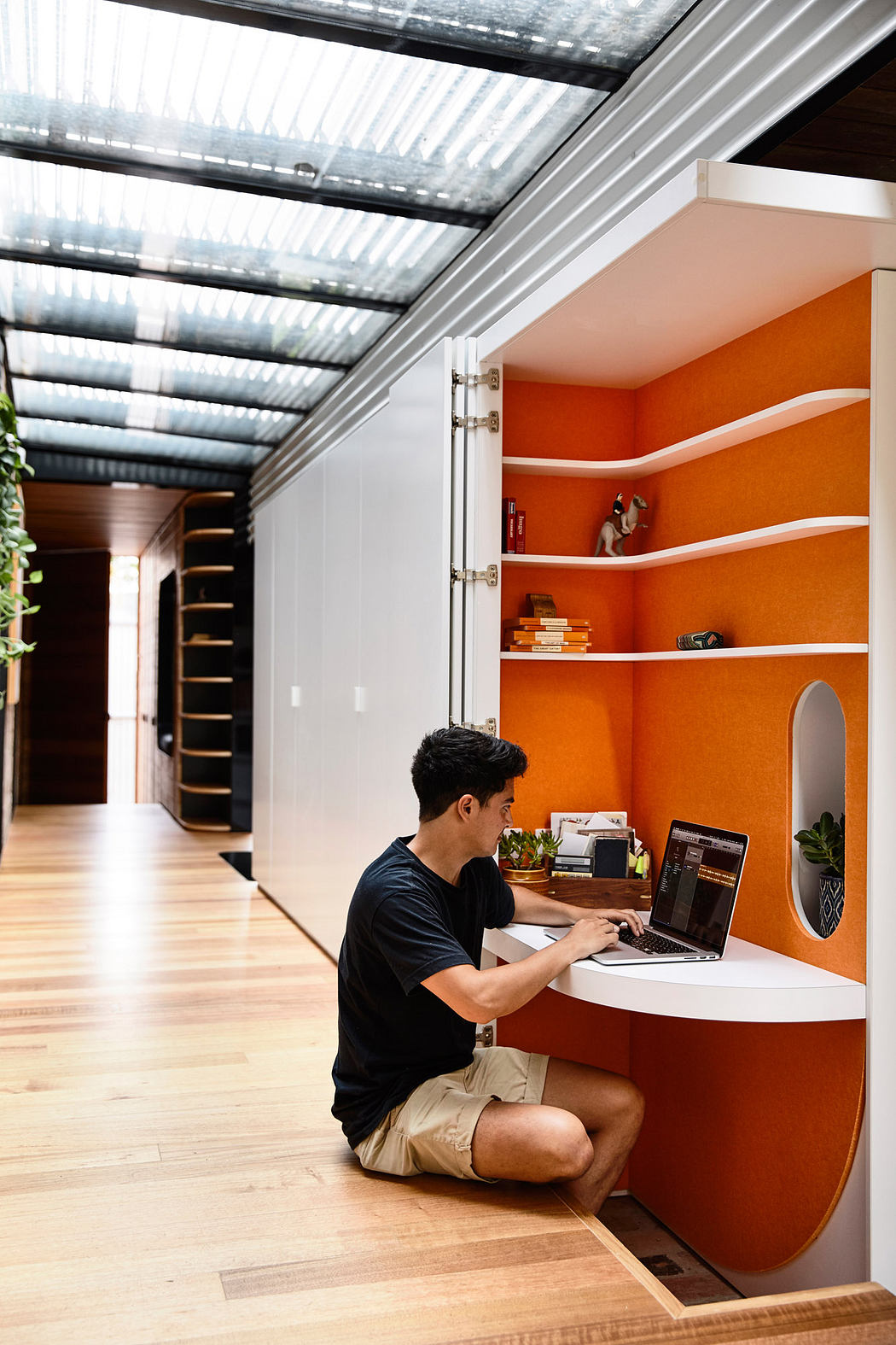 A vibrant orange nook with built-in shelves and a workspace, surrounded by a modern glass ceiling.