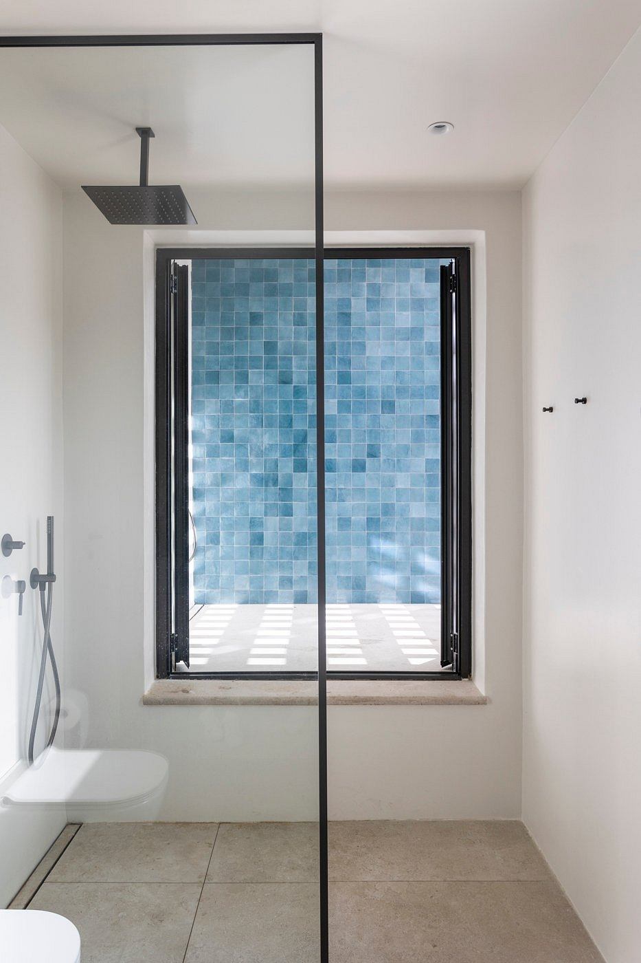 A modern bathroom with blue tiles, black accents, and a large window providing natural light.