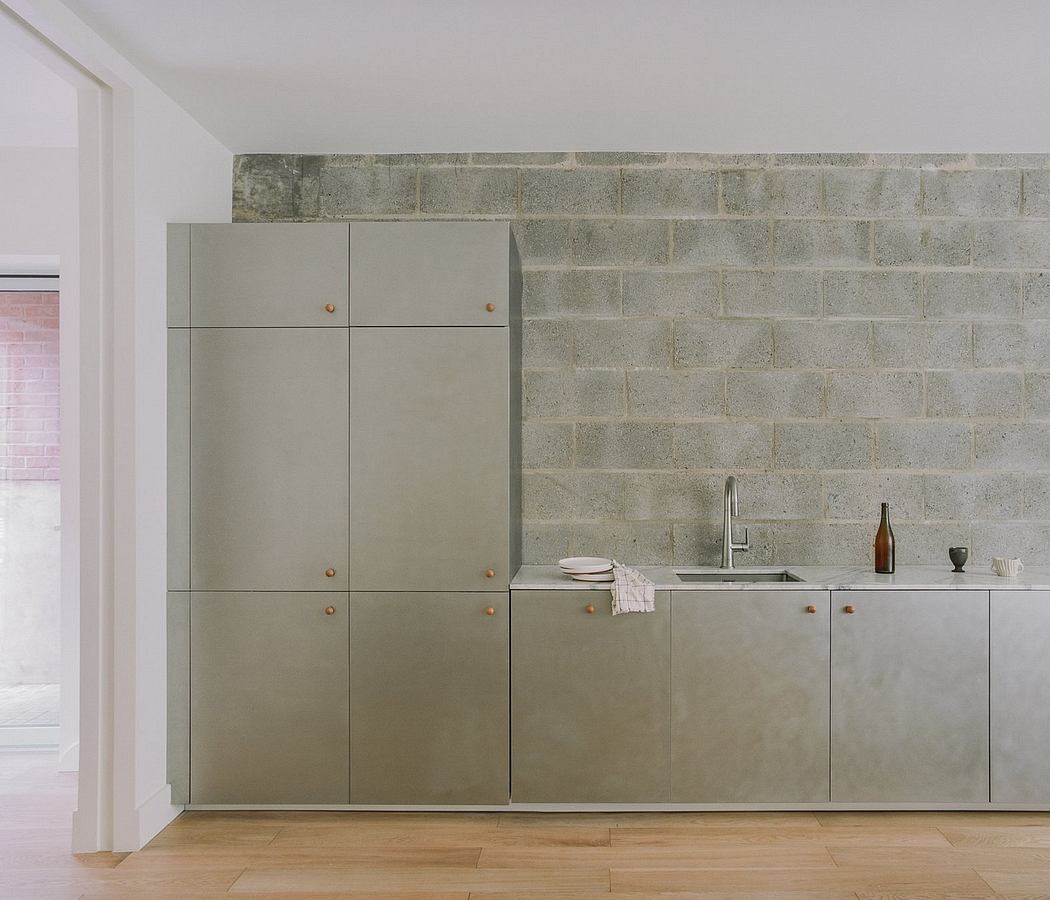 Minimalist kitchen design with concrete-look cabinets, wooden flooring, and brick walls.