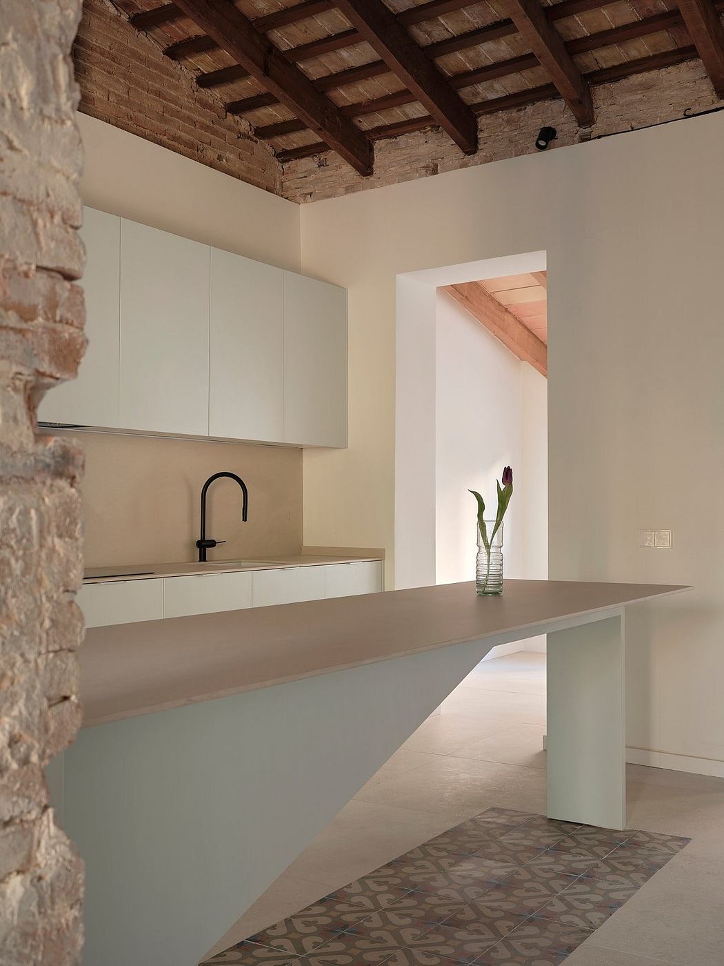 A modern kitchen with a sleek gray counter, wooden beamed ceiling, and patterned tile floor.