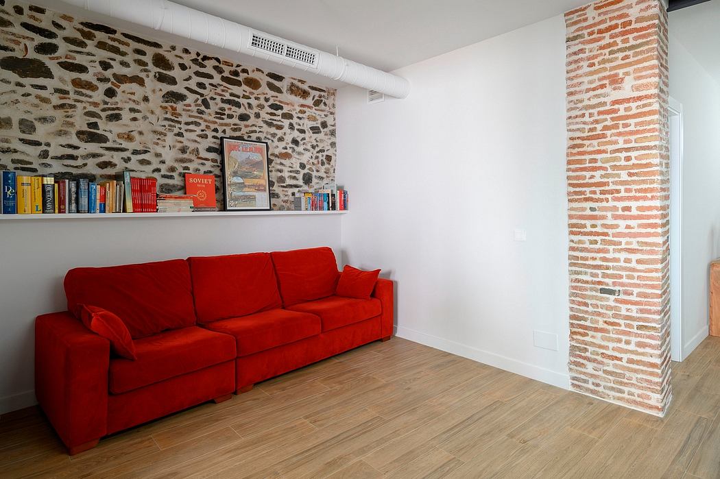 A cozy living room with a red sofa, exposed brick walls, and a floating shelf displaying books.