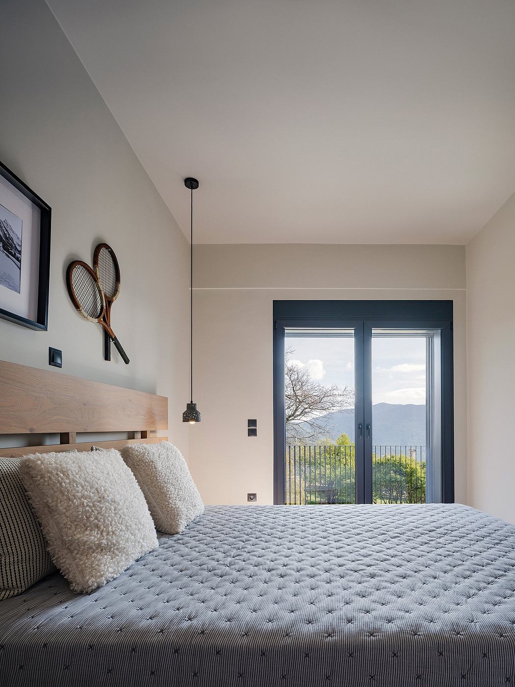 Modern bedroom with wooden headboard, plush bedding, and scenic mountain view through glass doors.