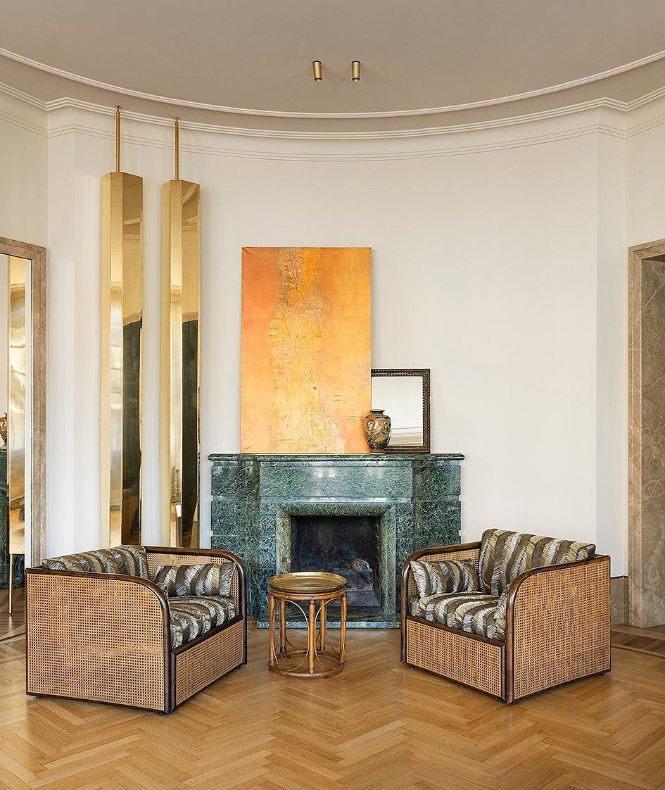 Curved white walls, brass lamps, marble fireplace, rattan furniture in a luxurious room.