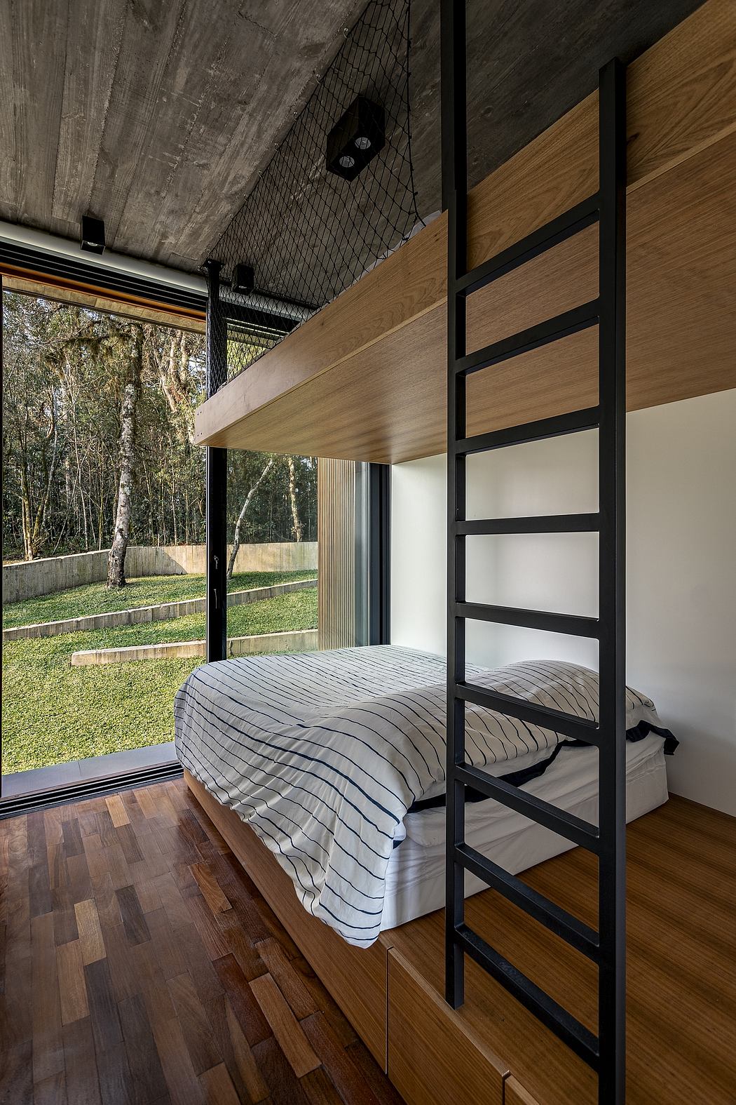 Modern bedroom with large windows overlooking a forested outdoor area, featuring a wooden platform bed and minimalist design.