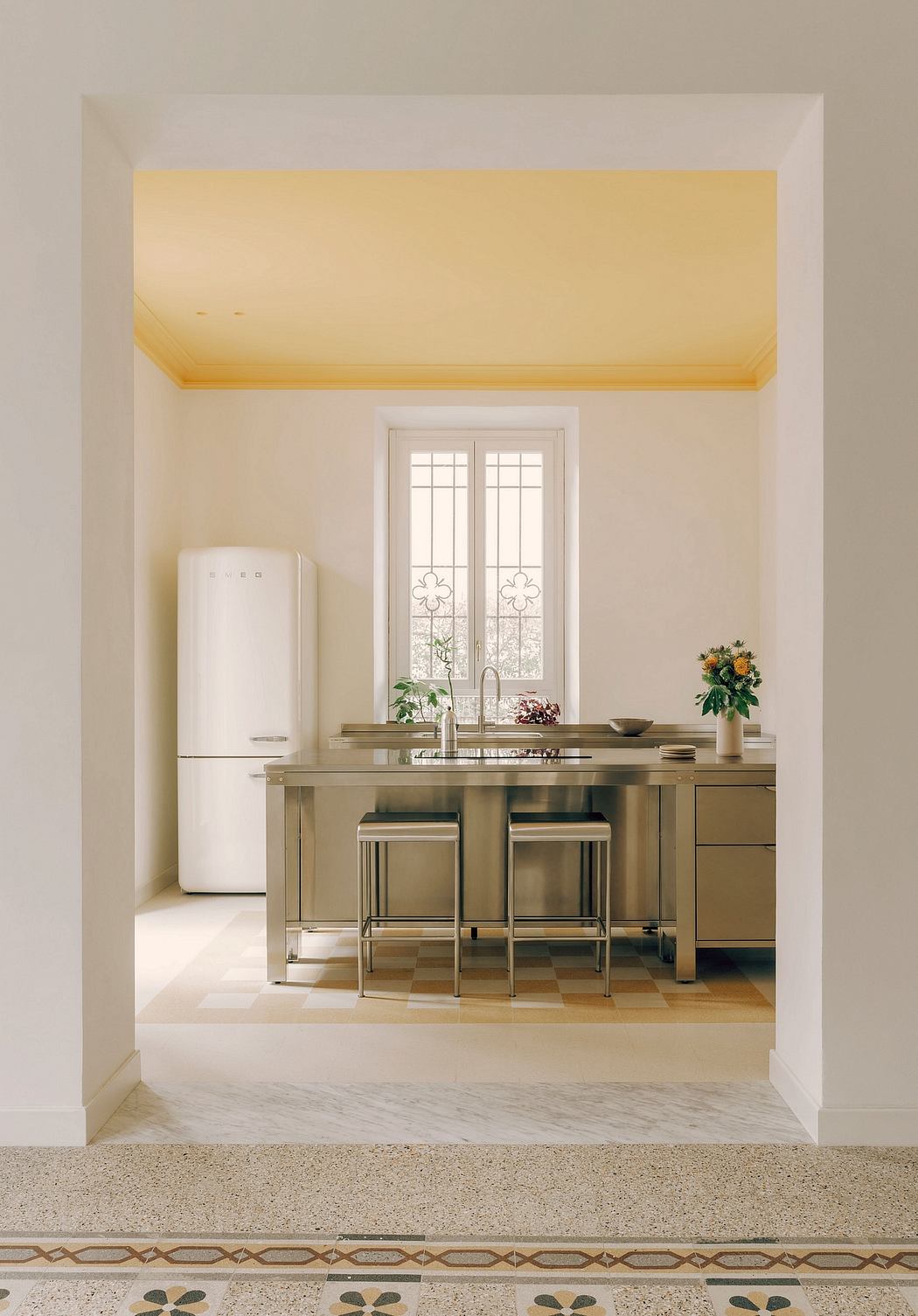 Bright kitchen with stainless steel island, vintage refrigerator, and ornate tile flooring.