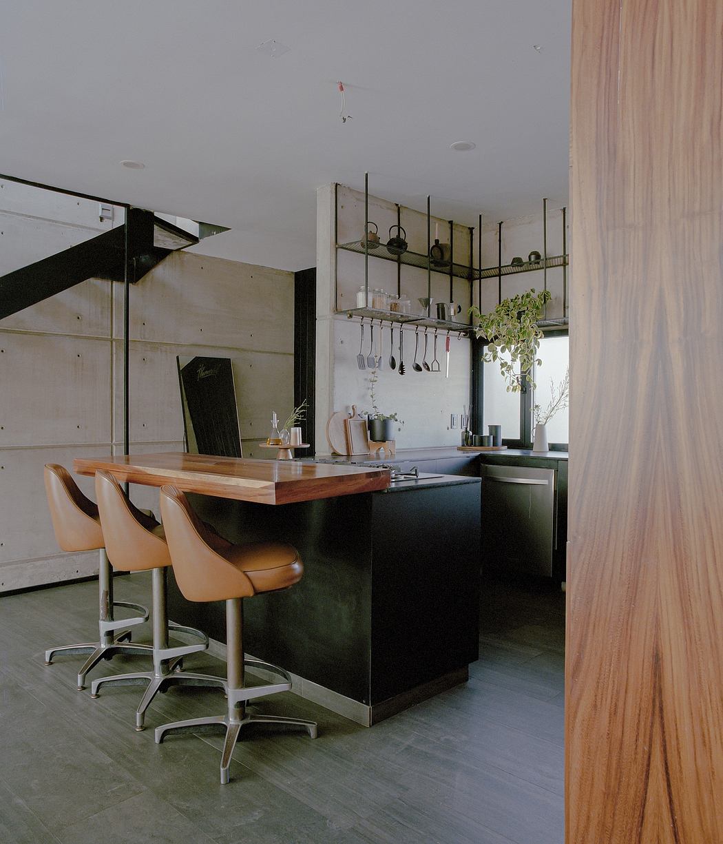 Modern, minimalist kitchen with sleek black cabinets, wooden countertop, and hanging storage racks.
