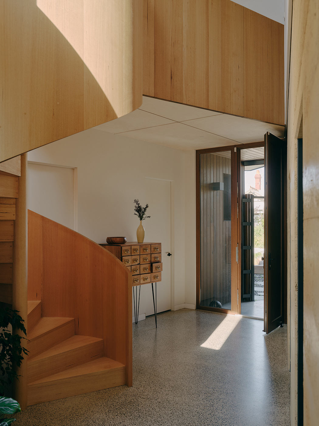 Warm wooden paneling, sleek staircase, and a glimpse of an outdoor space create a cozy ambiance.