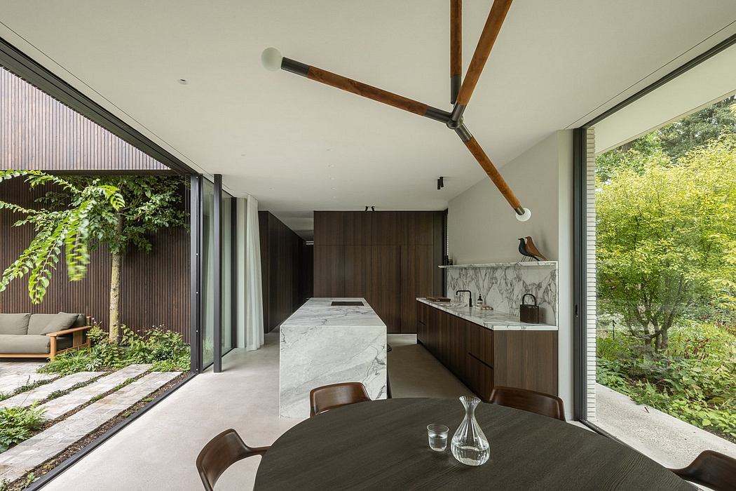 Modern, minimalist kitchen with marble countertop, wooden cabinets, and large window overlooking lush greenery.