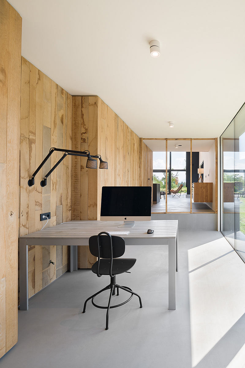 A contemporary home office with wooden paneling, minimalist desk, and large window.