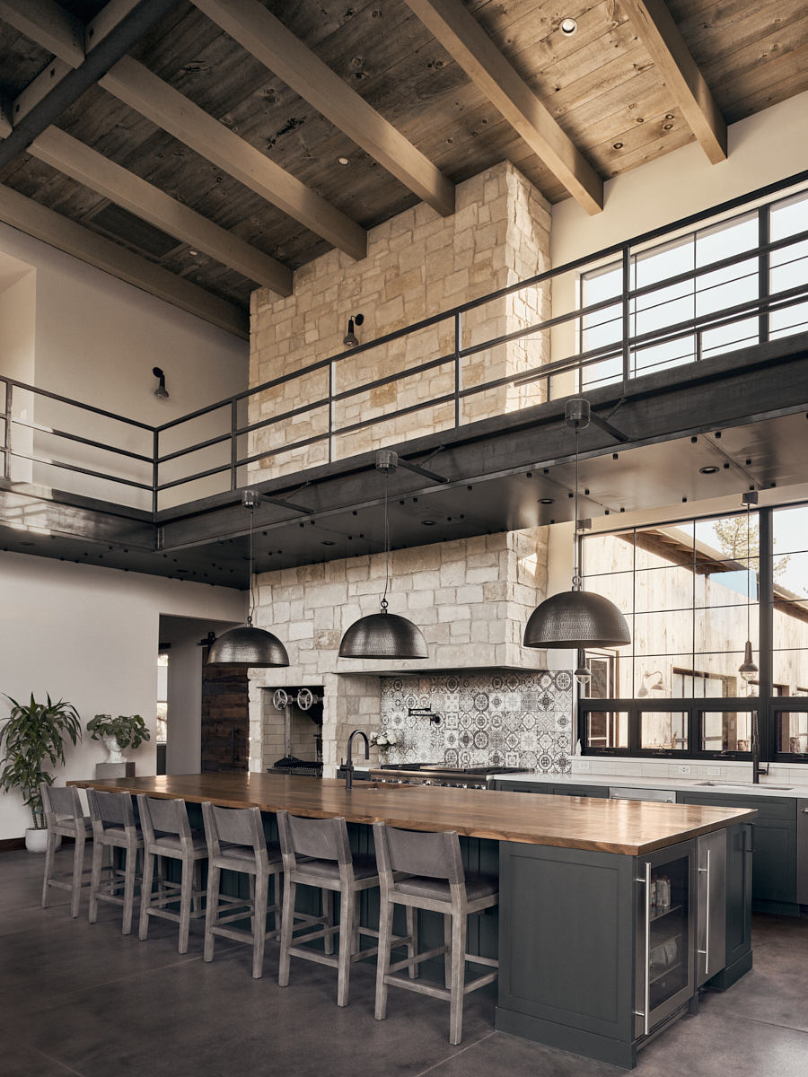 A modern rustic kitchen with exposed wooden beams, stone walls, and pendant lighting.