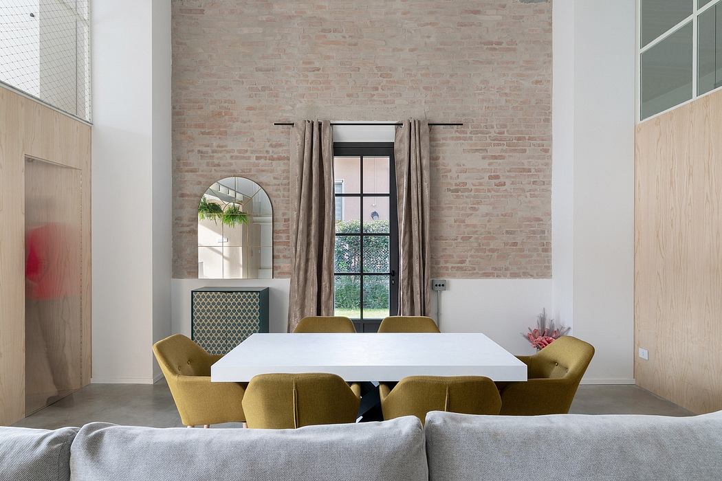 Bright open-plan dining area with exposed brick walls, arched mirror, and mustard-colored chairs.