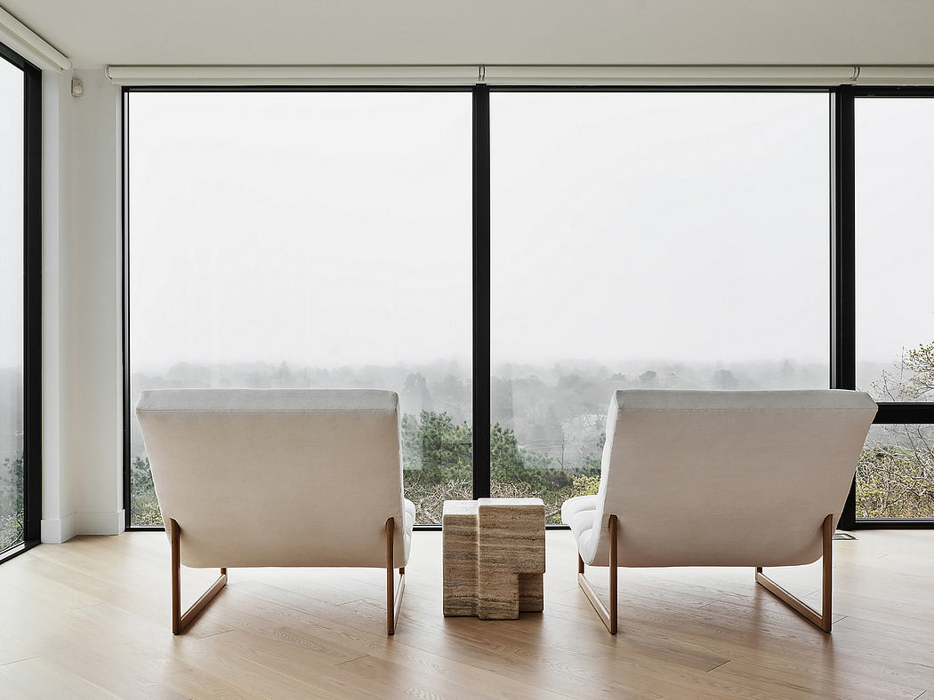 Minimalist living room with large windows, neutral-toned chairs, and wood accents.