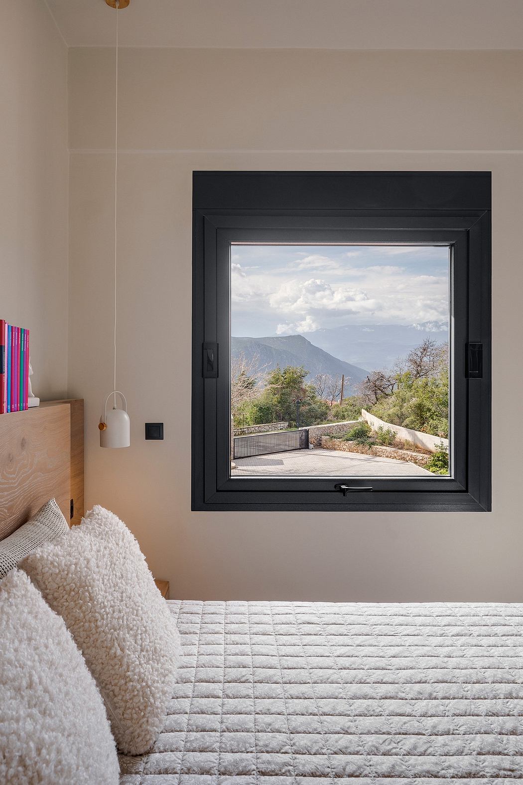A cozy bedroom with a large window framing a scenic mountain view, highlighting the architectural design.