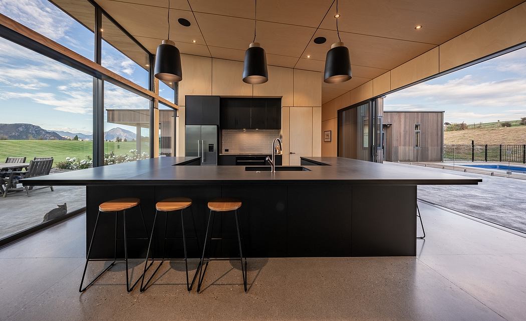 Modern kitchen with sleek black island, pendant lights, and floor-to-ceiling windows overlooking scenic landscape.
