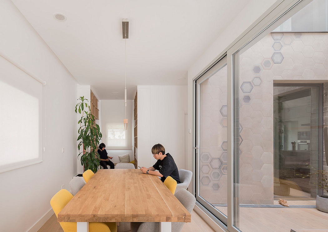 Modern open-concept interior with large windows, wooden dining table, and hexagonal patterned wall.