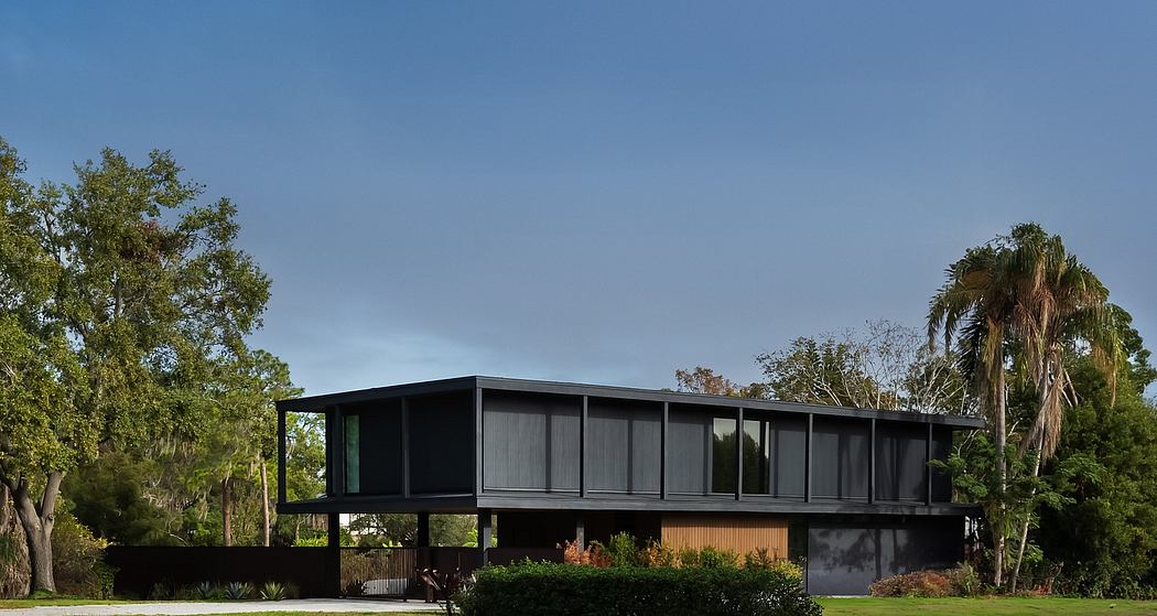 Sleek modern house elevated on stilts with expansive glass windows and lush vegetation.