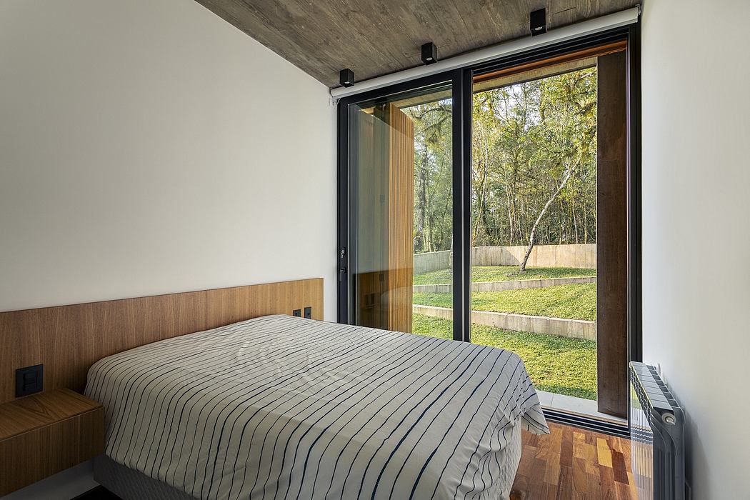 Minimalist bedroom with large sliding glass doors overlooking lush foliage.