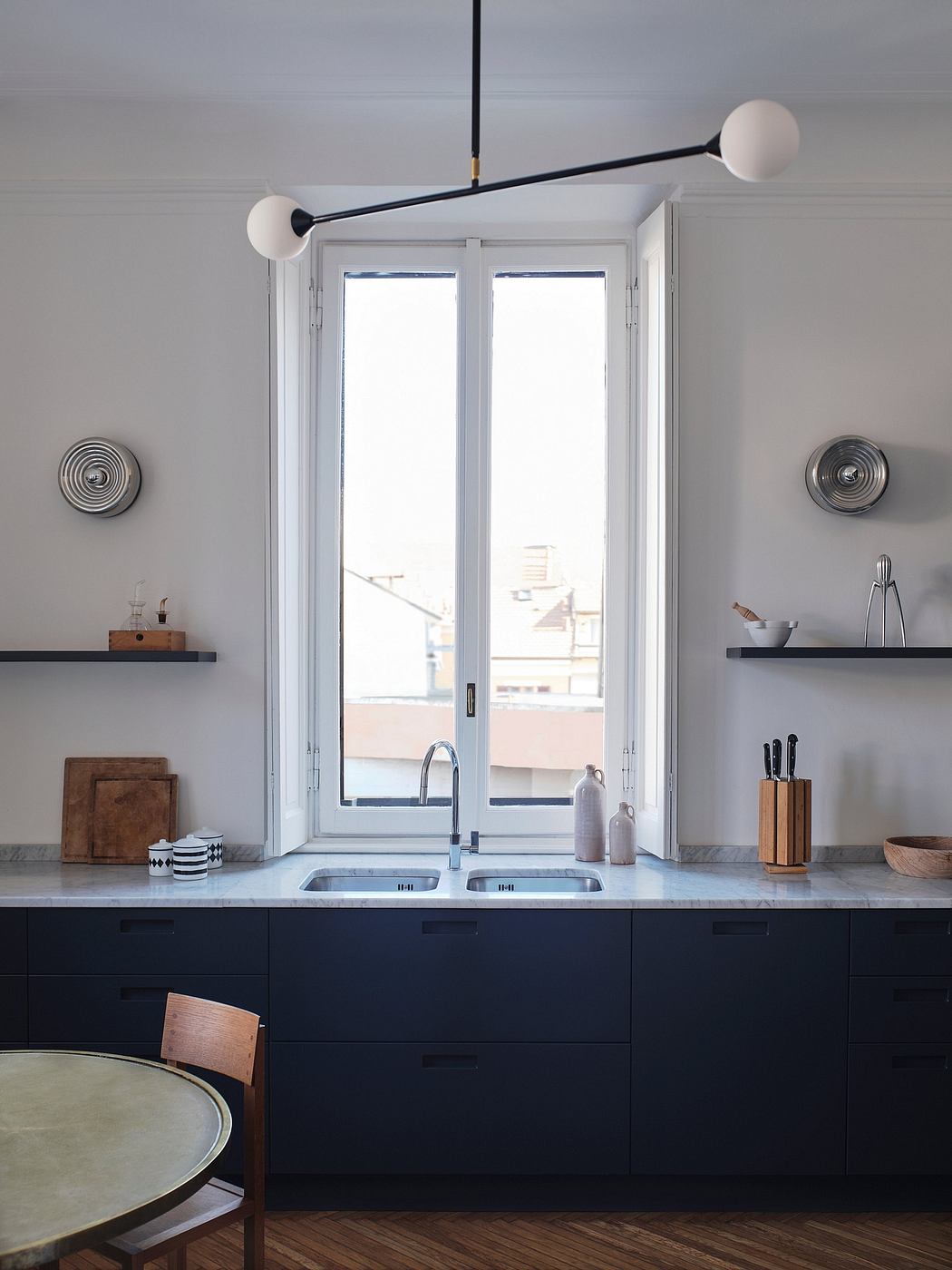 Minimalist kitchen with sleek black cabinetry, dual sinks, and a modern lighting fixture.
