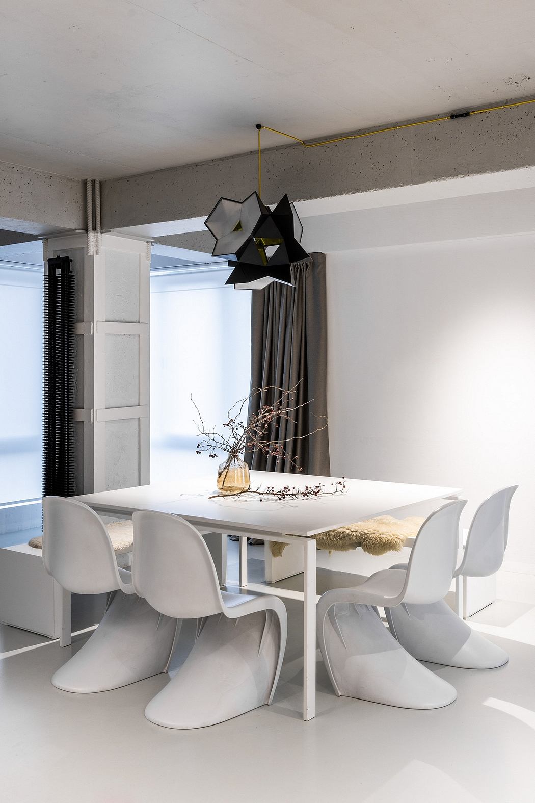 A modern dining area with a geometric light fixture and a plain white table and chairs.