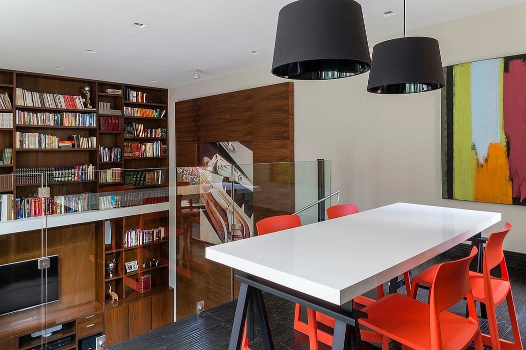 Modern and cozy interior with wooden bookshelves, white table, and vibrant red chairs.