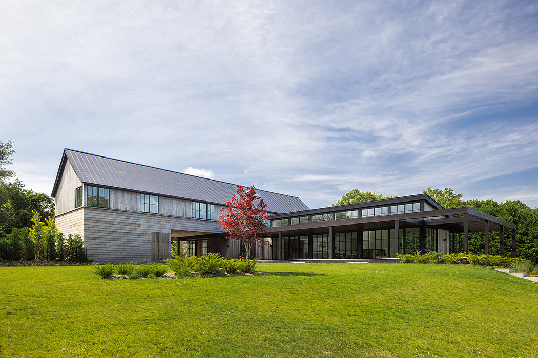 A modern, multi-level wooden house with large windows and a covered patio area surrounded by lush greenery.
