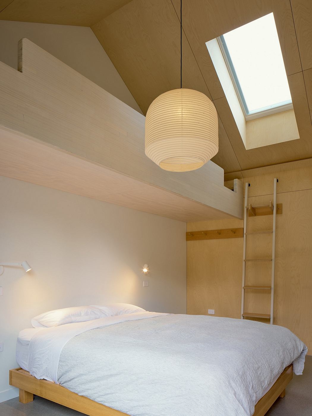 Minimalist bedroom with wood-paneled walls, slanted ceiling, and a round paper lantern light fixture.