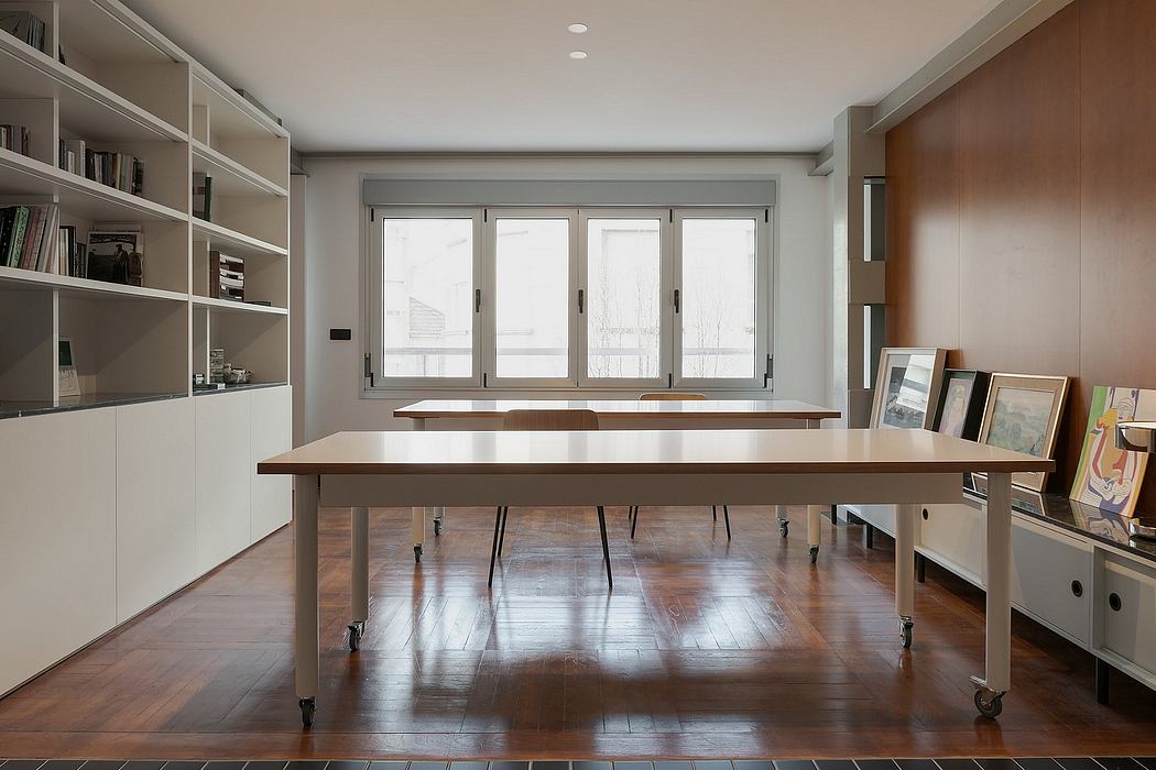A spacious, minimalist home office with large windows, built-in shelves, and a wooden table on wheels.
