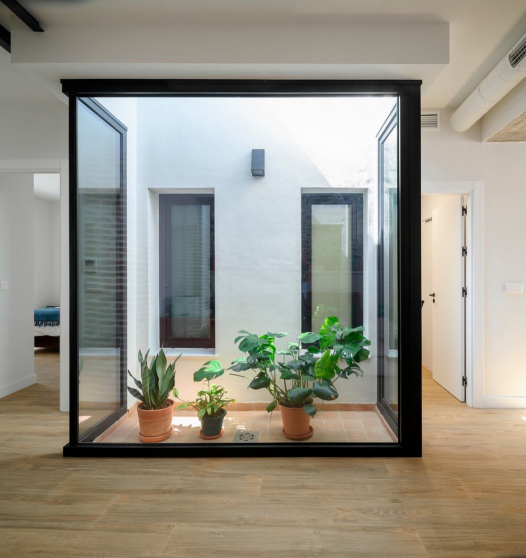 An interior room with a large glass window frame, displaying potted plants and a wooden floor.