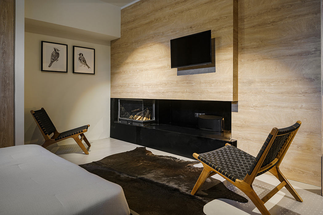A cozy bedroom with a wood-paneled accent wall, fireplace, and mid-century modern chairs.