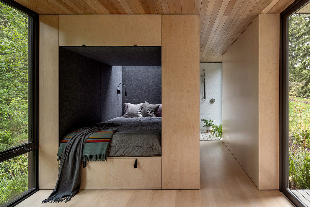 A cozy, minimalist bedroom with a built-in bed niche, surrounded by wooden walls and views of the forest.