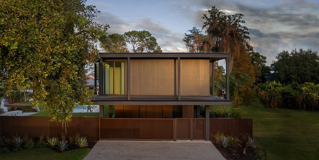 Modern two-story wooden house with glass walls and metal roof surrounded by trees.