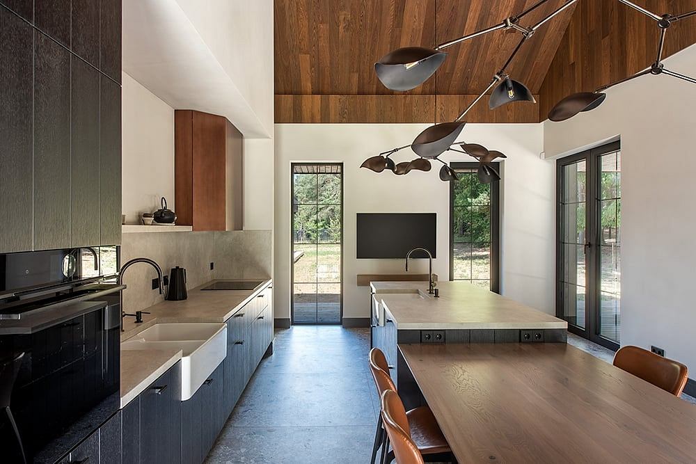 Modern kitchen with wooden ceiling, concrete countertops, and a large dining table.